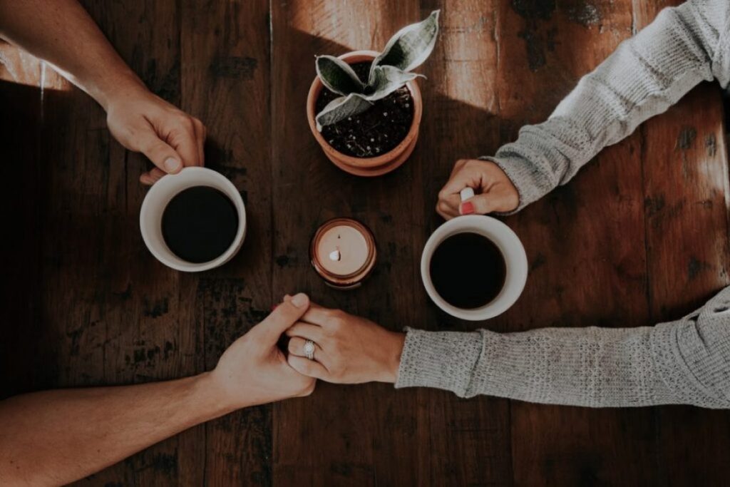 couple holding hands at table with coffee mugs