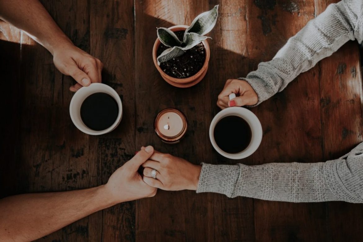 couple holding hands at table with coffee mugs